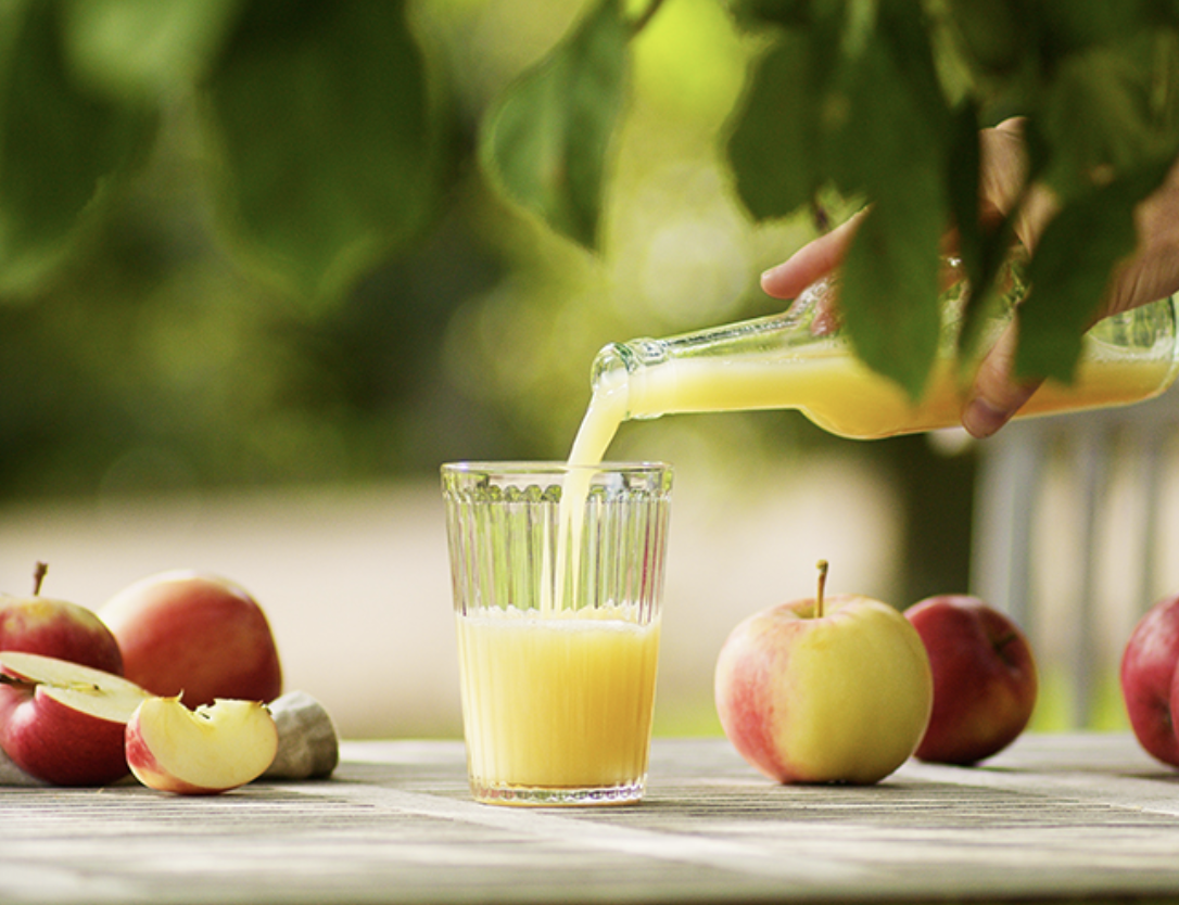 Äpplen på ett bord. En hand häller upp cider från en flaska