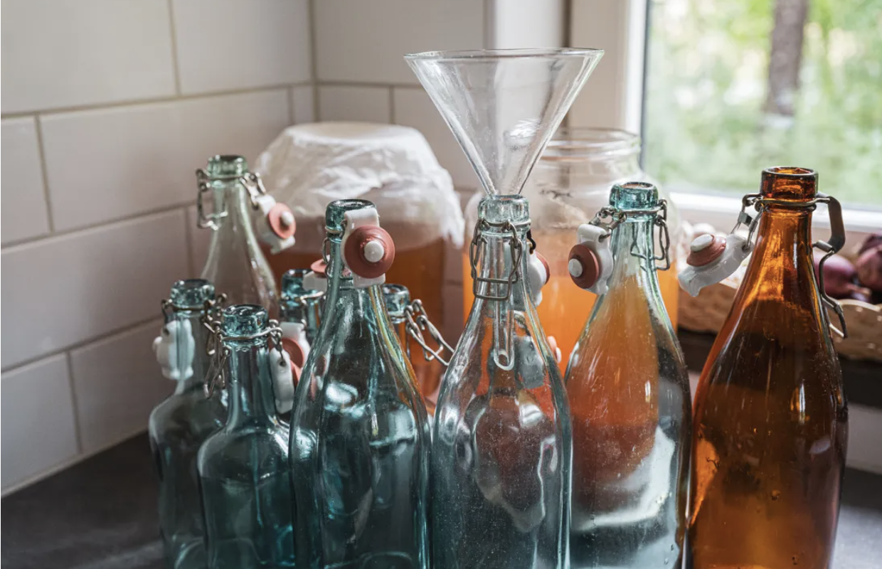 Tomma ciderflaskor med ciderutrustning i bakgrunden.